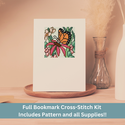 Cross-stitch greeting card featuring a monarch butterfly on a pink flower, stitched on Aida cloth.