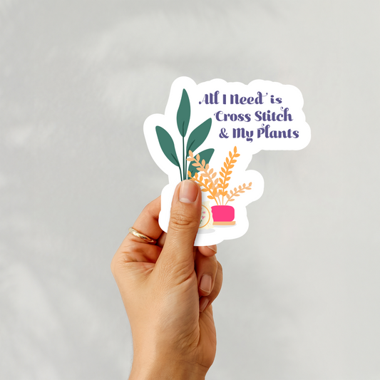 Hand holding a “All I Need is Cross Stitch & My Plants” sticker with potted plants and hoop design
