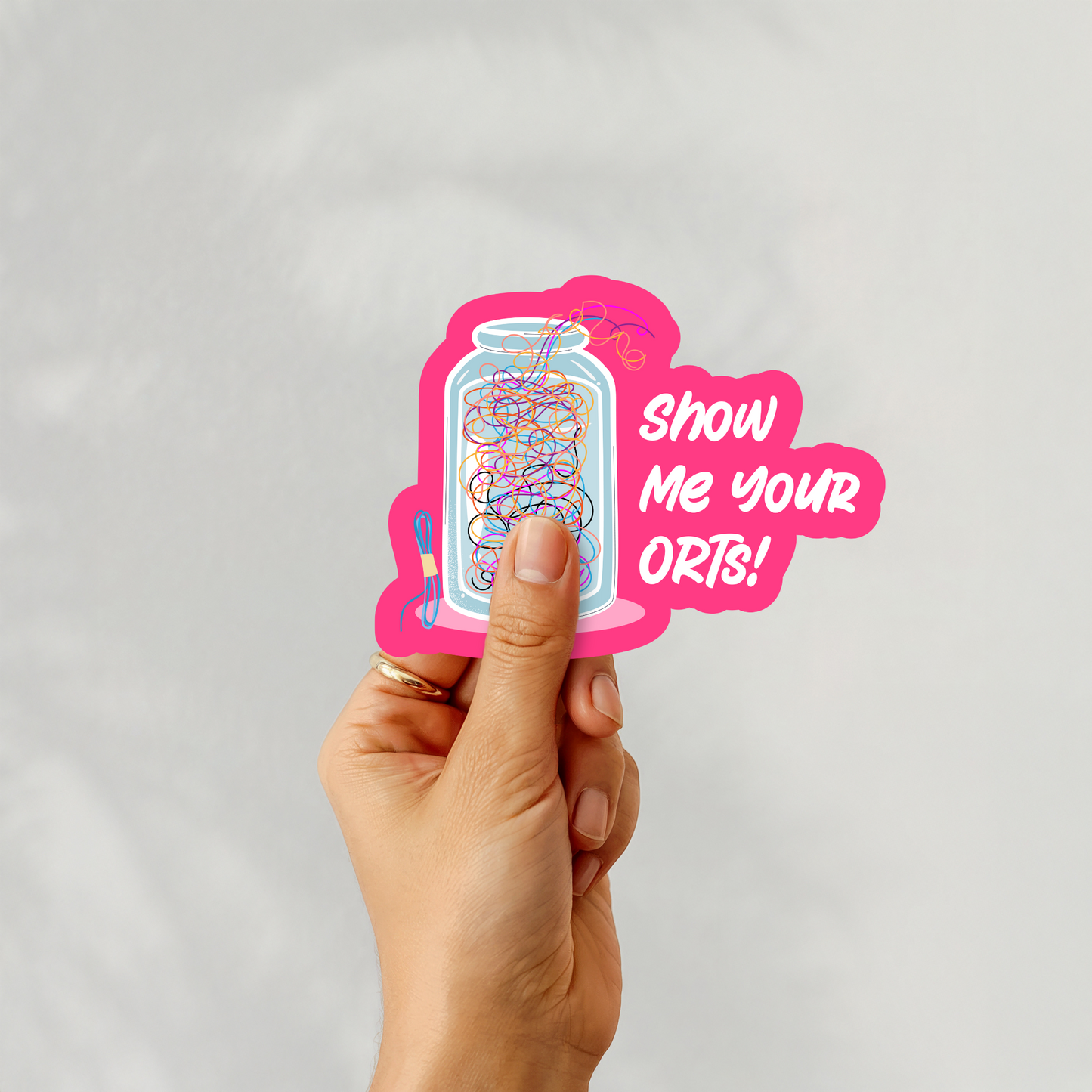 Hand holding ‘Show Me Your ORTs!’ sticker with jar of thread snippets and playful text
