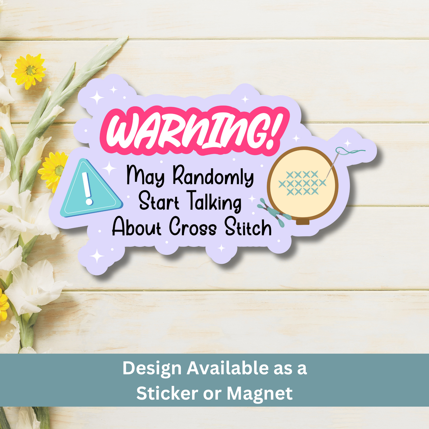 A cross stitch-themed magnet with a bright warning sign placed on a wooden surface